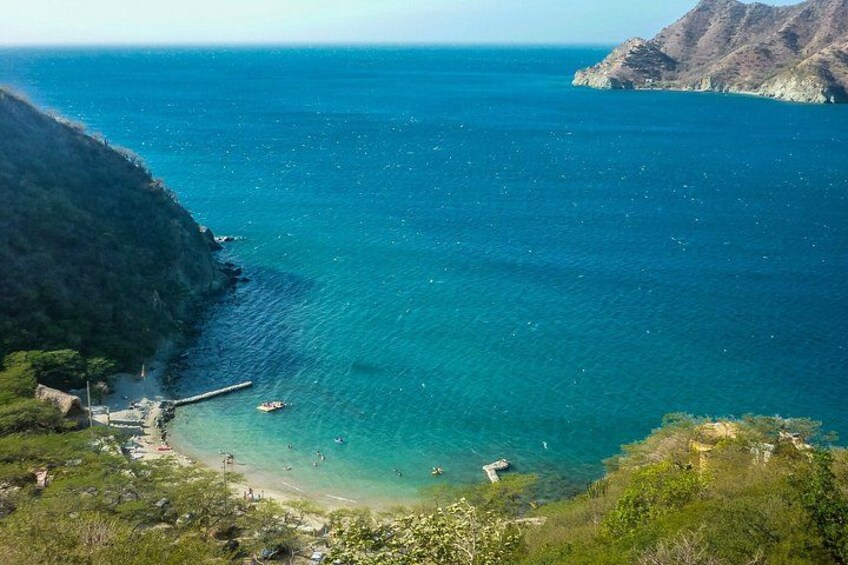 A coastal landscape with a clear blue sea, a rocky shoreline, and a small pier extending into the water. 2