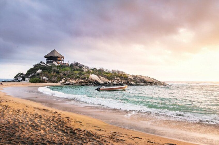 A beach with a hut on a rocky outcrop, a boat near the shore, and waves gently lapping the sand. 1