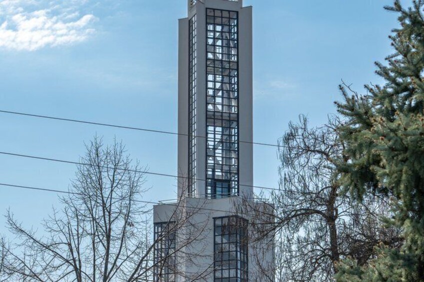 Ein hohes Gebäude mit einer gitterartigen Fassade, umgeben von baumlosen Bäumen und einem klaren Himmel. 3