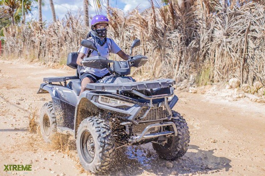 A person riding an ATV on a dirt path with dry vegetation in the background. 1