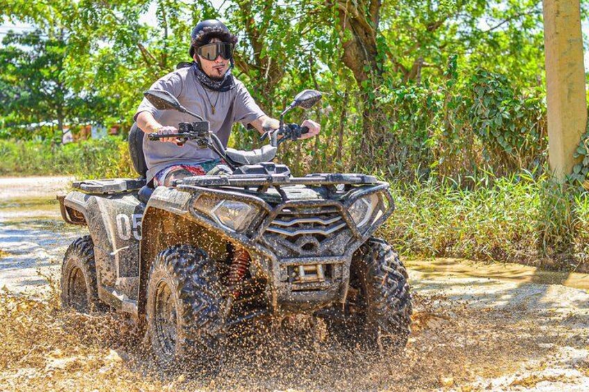 A person riding an ATV through a muddy path surrounded by greenery. 2