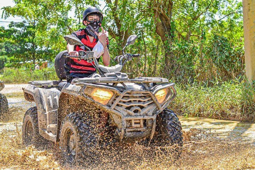 A person riding an ATV through a muddy area with splashes of mud around. 2