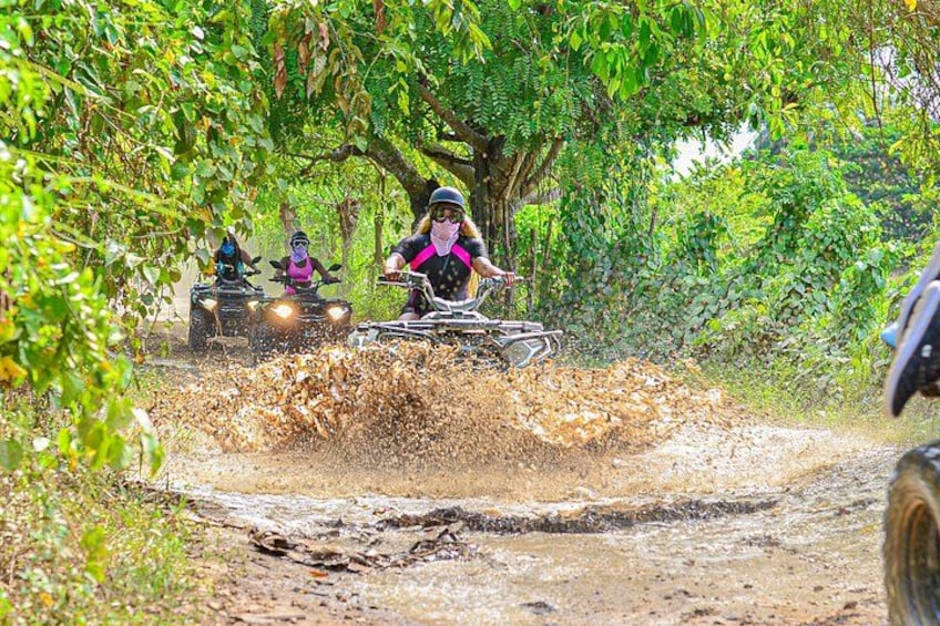 People riding ATVs on a muddy trail surrounded by trees. 4
