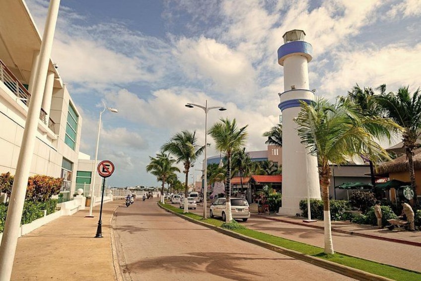 A street with a white lighthouse, palm trees, and a building with a red roof. 5
