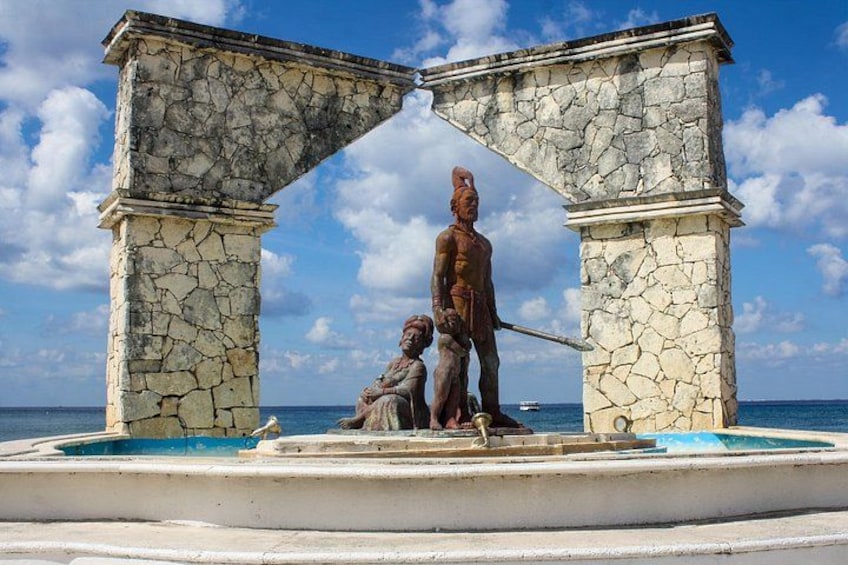 A statue of a man holding a spear, standing between two stone pillars, with a body of water in the foreground. 2
