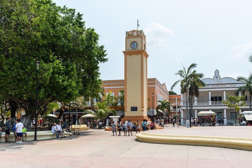 A public square with a clock tower, palm trees, and people walking. 1