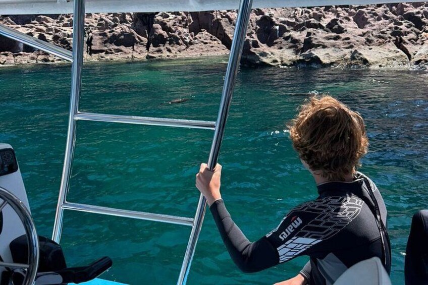 A person in a wetsuit on a boat, holding onto a ladder. 2