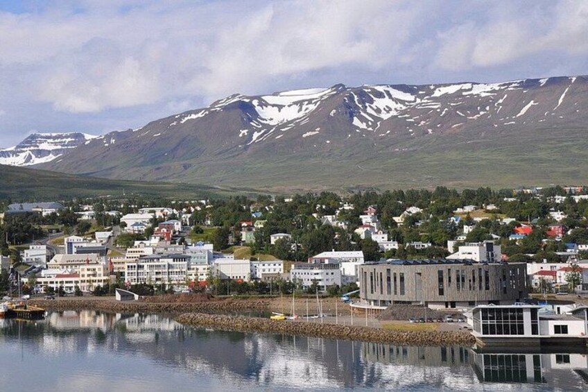 A coastal town with buildings, a calm body of water, and snow-capped mountains in the background. 4