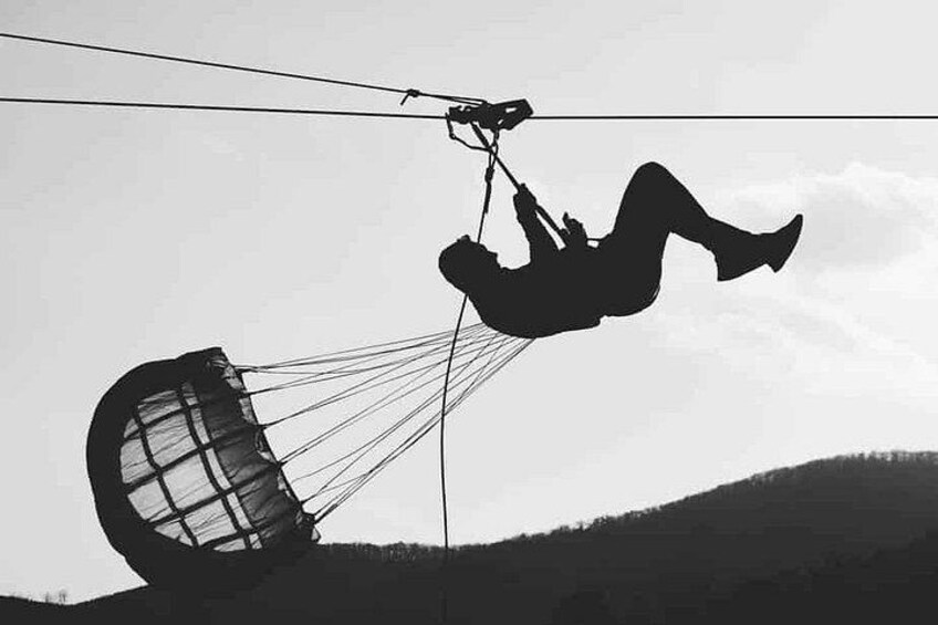 A person paragliding with a parachute, suspended by a cable. 4