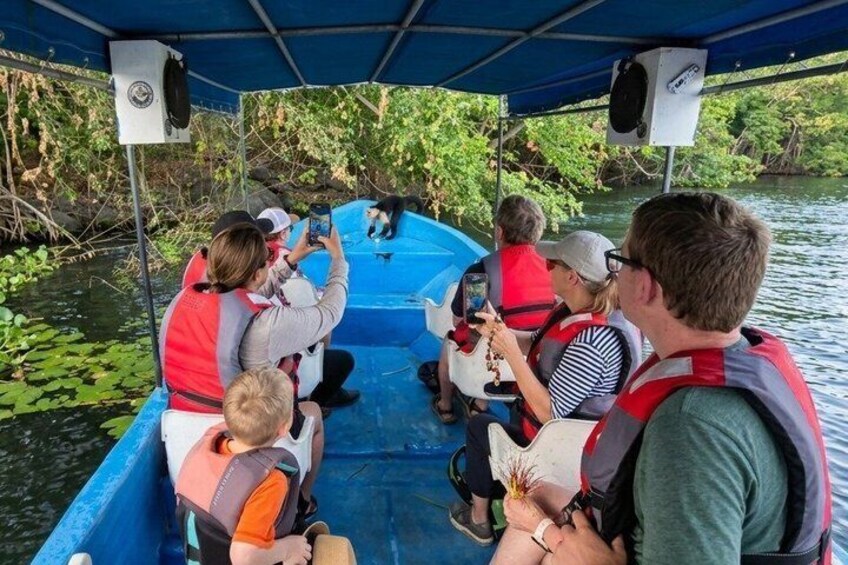 A group of people on a boat, wearing life jackets, with a water body and greenery in the background. 4