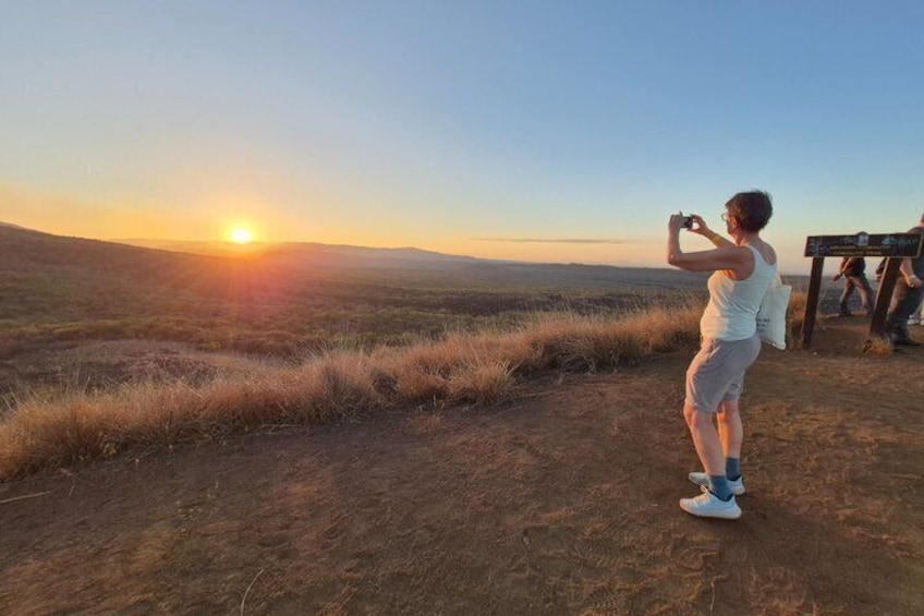 A person taking a photo of the sunset with a landscape in the background. 1