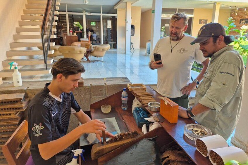 A person preparing food at a counter with a phone, another person standing nearby, and a staircase in the background. 2