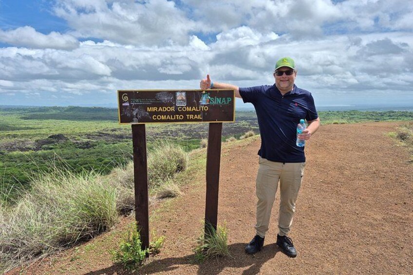A person standing next to a trail sign for the Mirador Comalito Trail. 5