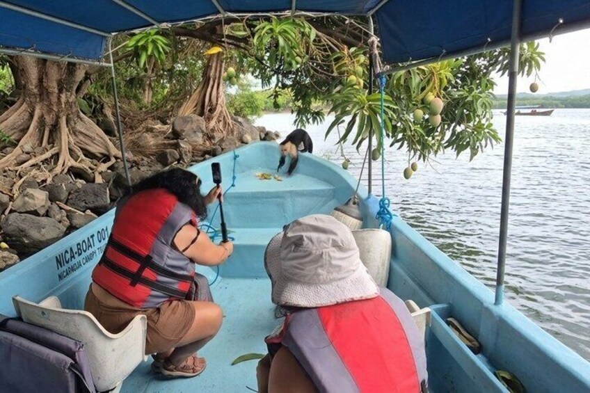 A boat with people wearing life jackets, a microphone, and a camera, surrounded by trees and water. 2