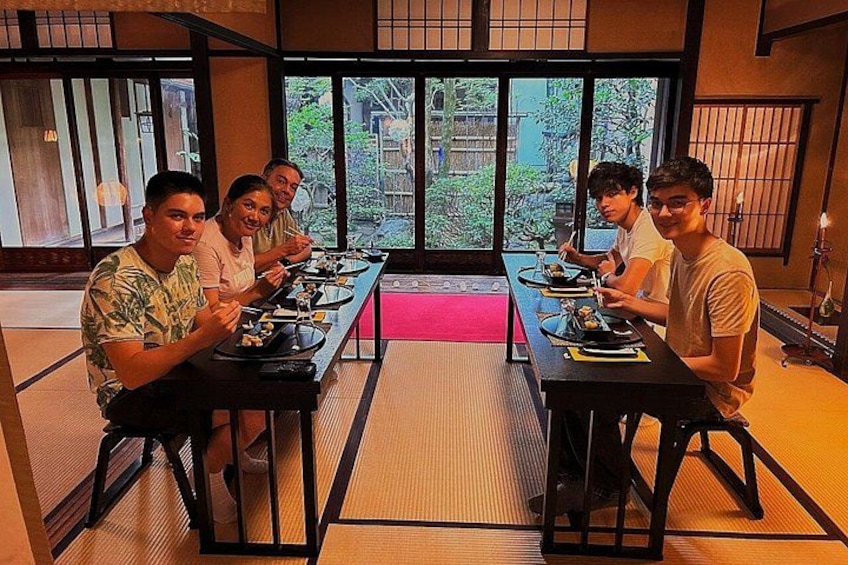 A group of people seated at a long table in a traditional Japanese room with tatami flooring and sliding doors. 2