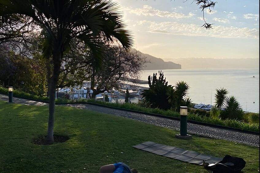 A coastal landscape with a grassy area, a paved path, and a view of the sea and distant hills. 3