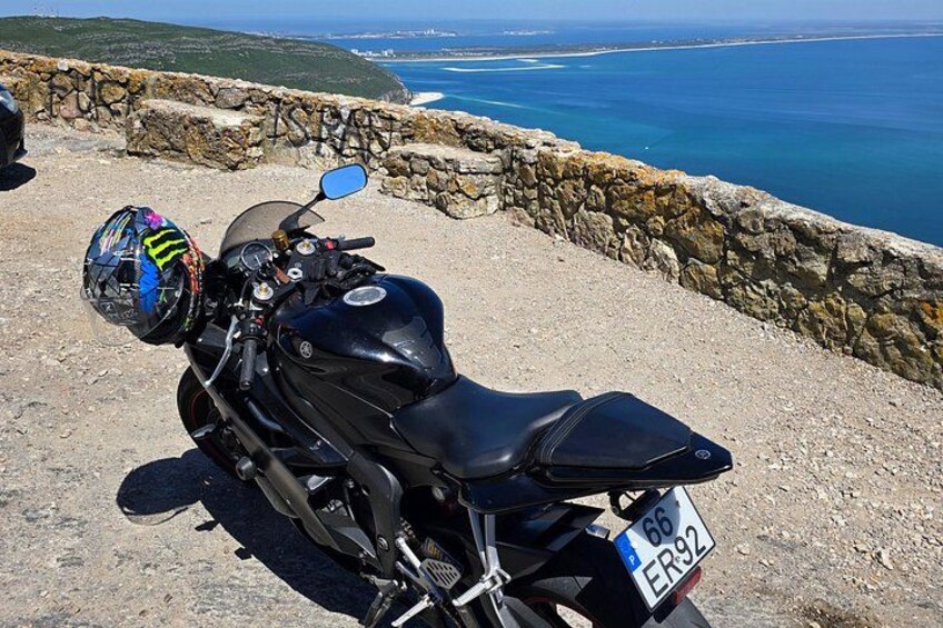 A black motorcycle parked on a rocky seaside path with a stone wall and ocean view. 5