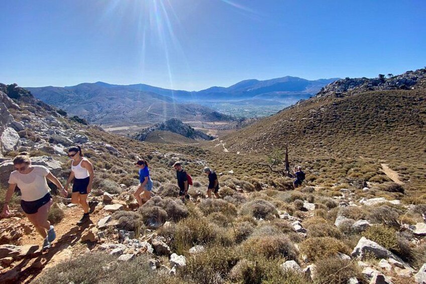 A group of people hiking on a rocky trail with a mountainous landscape in the background. 1