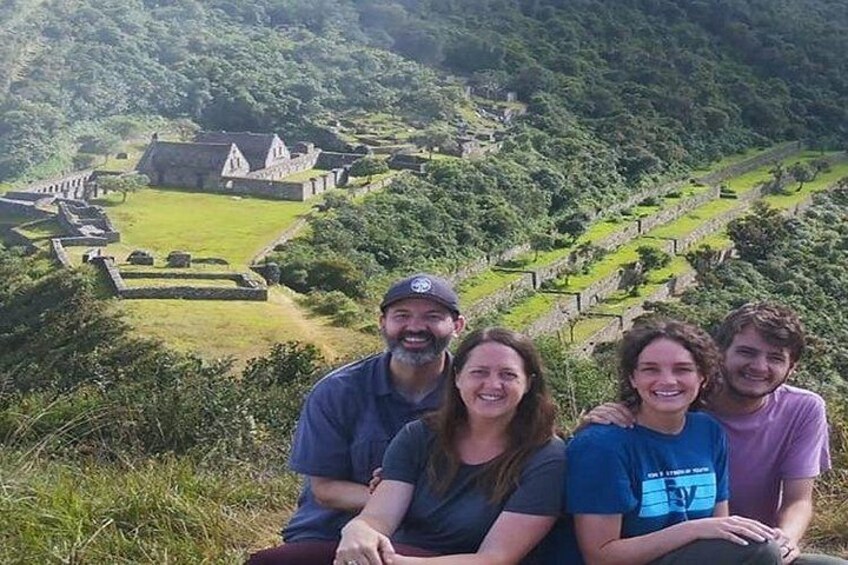 A group of people sitting on a grassy hill overlooking a historical site with ruins and terraced fields. 5