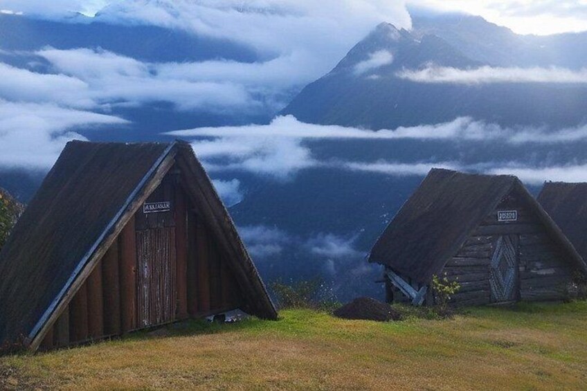 Two wooden huts with signs, surrounded by a mountainous landscape and clouds. 4