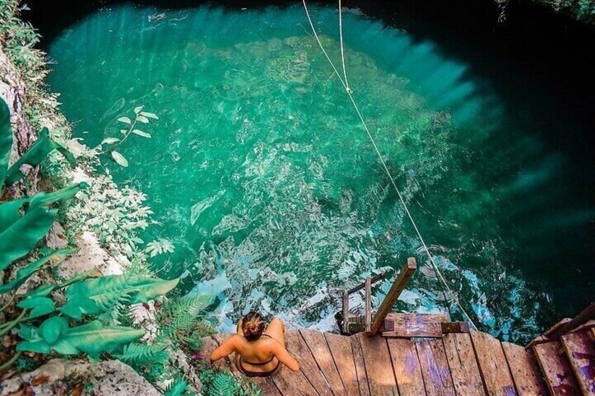 A person sitting on a wooden platform overlooking a clear blue water body surrounded by greenery. 5