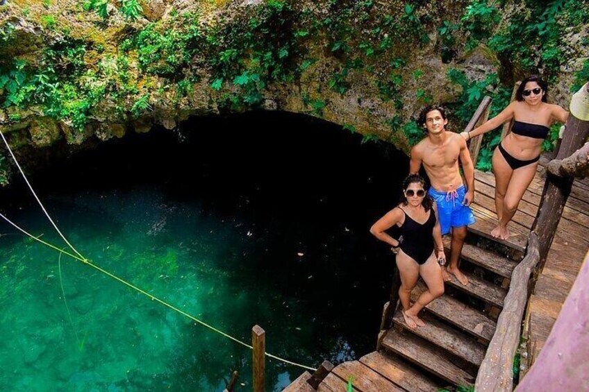 A natural pool with clear water, surrounded by greenery and a wooden staircase. 1