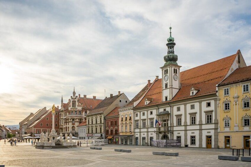 A historic square with buildings, a clock tower, and a fountain. 1