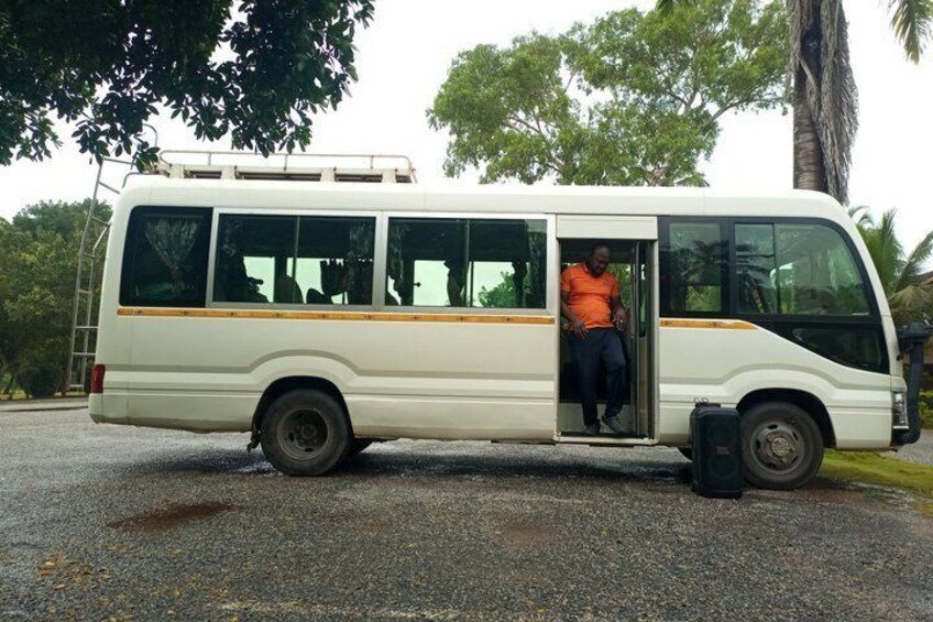 A white bus with an open door, parked on a gravel surface with trees in the background. 5