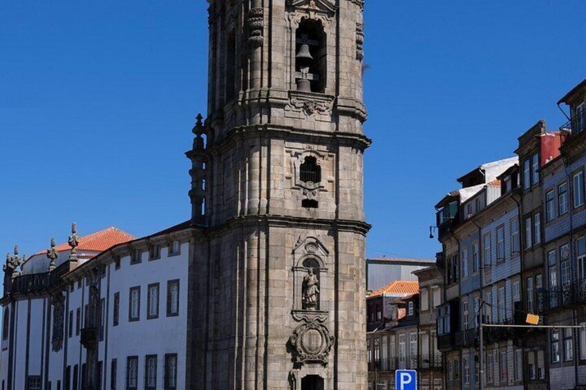 Una torre histórica con tallados intrincados y una campana, rodeada de edificios con tejados de tejas rojas. 2