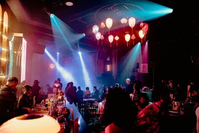 A crowded indoor venue with tables, people, and a stage with musical instruments. 4