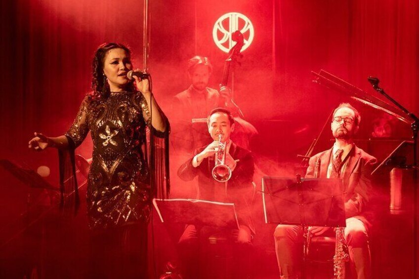 A person singing on stage with a saxophone and piano in the background. 2