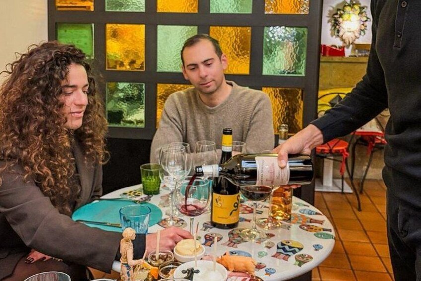 A dining table with wine glasses, bottles, and a person pouring wine. 5