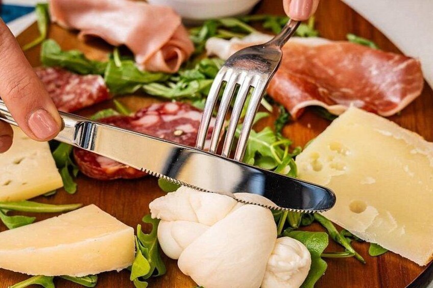 A variety of cheeses, cured meats, and leafy greens on a wooden board. 3