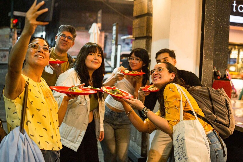 A group of people holding red plates with food, standing in an urban setting at night. 1