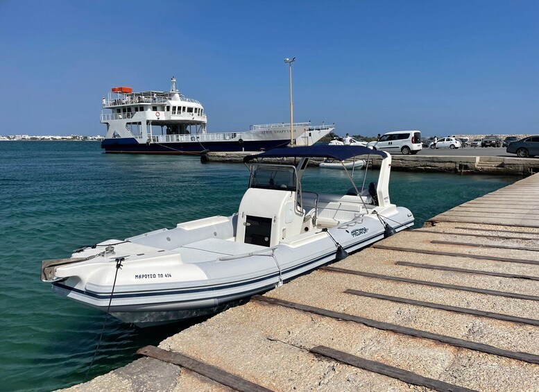 A small white boat docked at a pier with a larger vessel in the background. 3