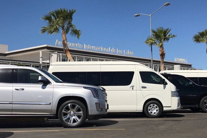 A parking lot with several vehicles, including a white SUV and a white van, in front of a building with palm trees and a clear blue sky. 3