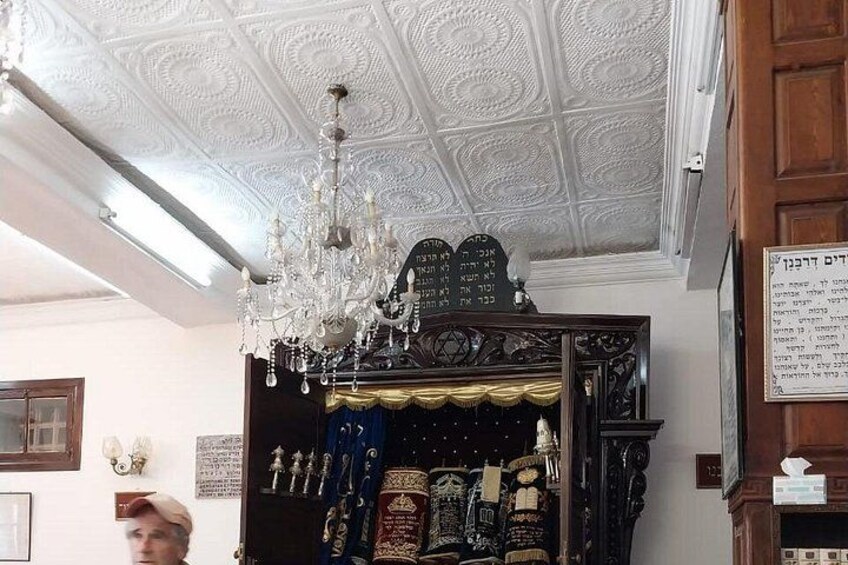 A room with ornate ceiling, a chandelier, and a display case with items. 2