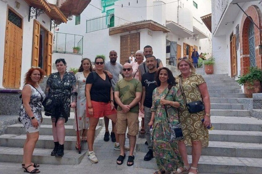 A group of people standing on stone steps in a narrow street with white buildings and wooden doors. 1