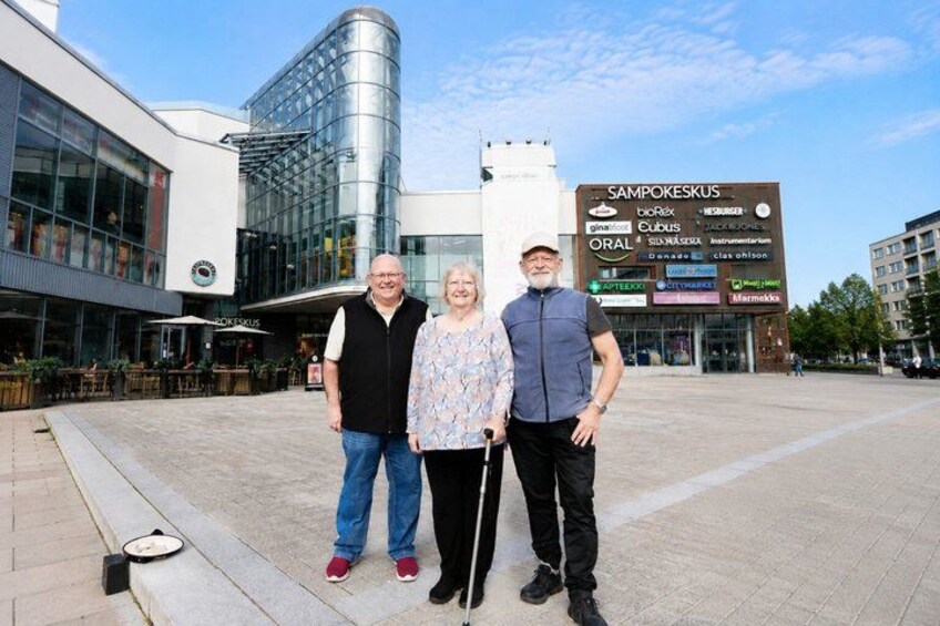 Three people standing in front of a modern building with a signboard. 4