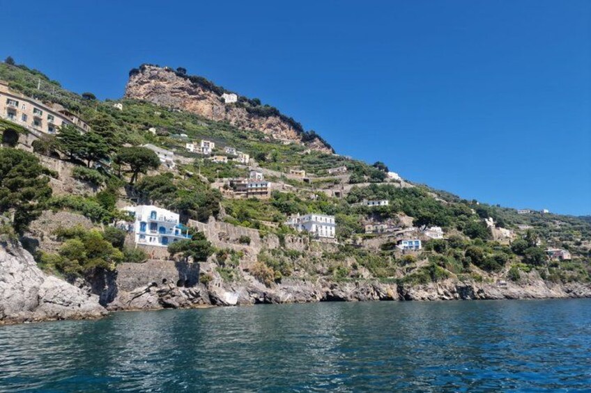 Un pueblo costero con edificios en una ladera, un litoral rocoso y un cielo azul despejado. 3