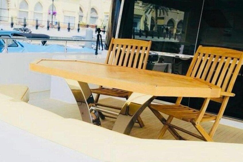 Mesa y sillas de madera en un balcón con vista a un edificio y autos estacionados. 3