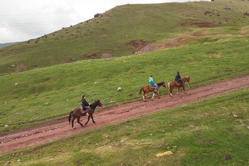 Three people riding horses on a dirt path in a hilly area. 4