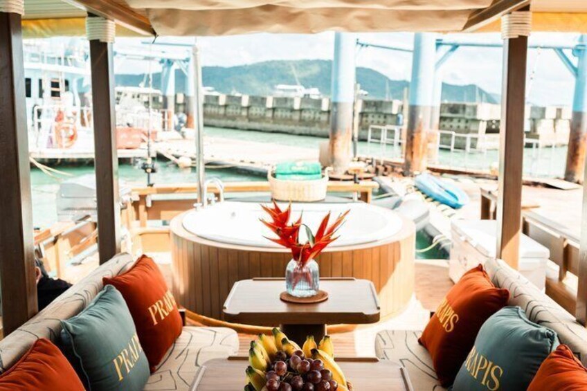 Un pont de bateau avec une table ronde, des coussins et un vase rempli de fleurs rouges. 4