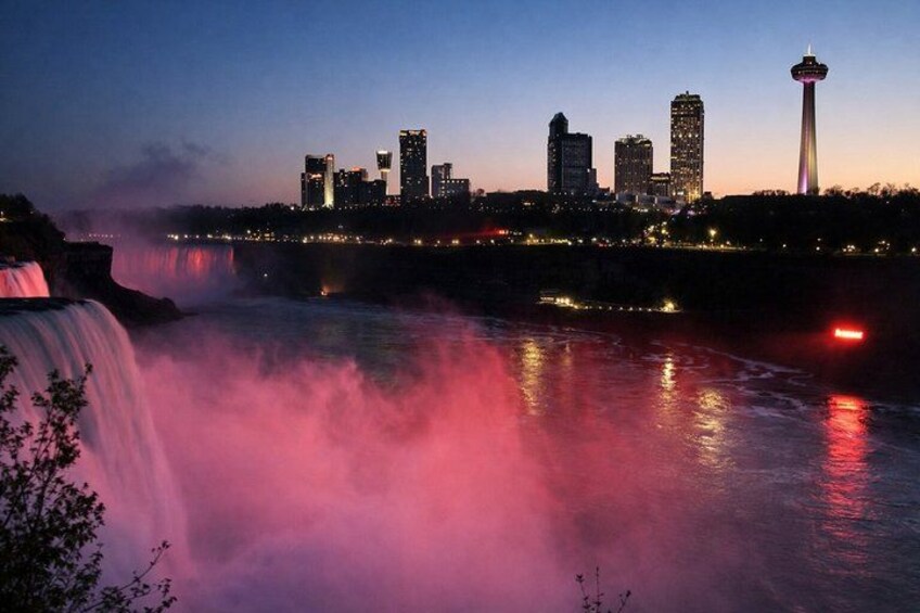 A city skyline with a prominent tower, a waterfall, and illuminated buildings at dusk. 2