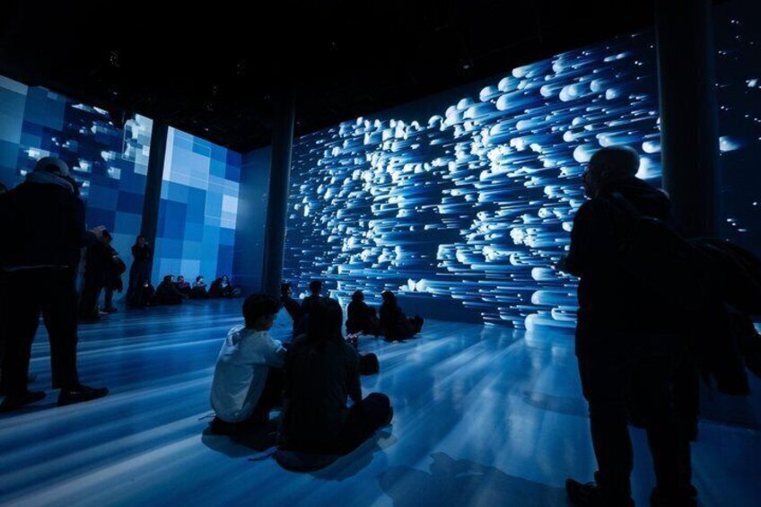 A group of people observing a large, illuminated sculpture installation in an indoor space. 5
