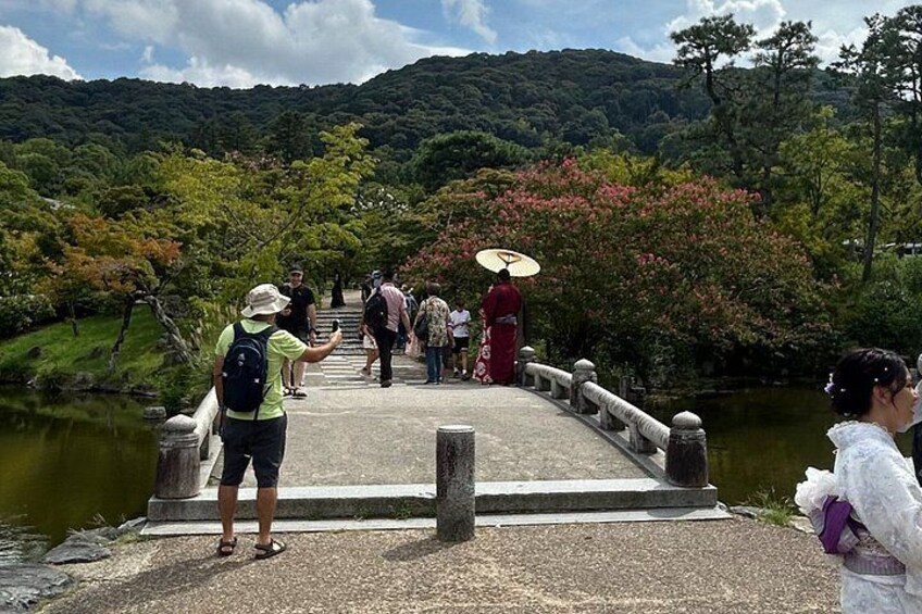 A bridge over a river with people walking, surrounded by greenery and hills. 5