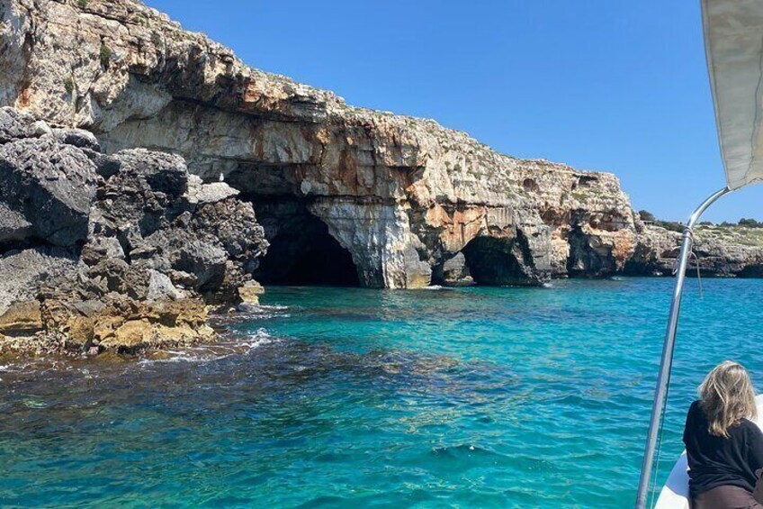 A rocky coastline with a cave entrance and clear turquoise water. 5