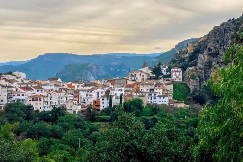 A village nestled in a valley with white buildings, surrounded by greenery and mountains. 1