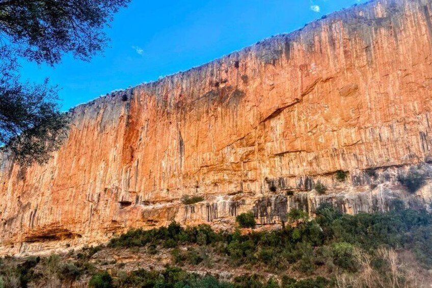 A large red rock cliff with sparse vegetation at its base. 4