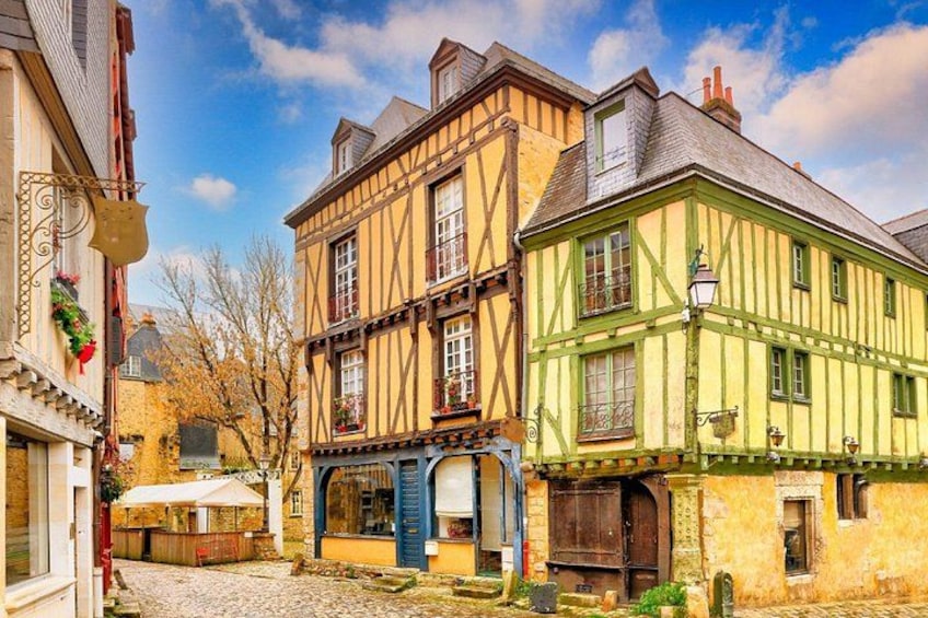 A cobblestone street with traditional half-timbered houses, a shop with a blue awning, and a clear blue sky. 2